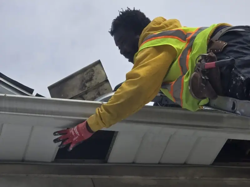Technician reaching up to an open gap under a gutter